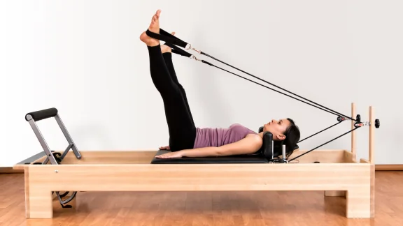 Woman performing a controlled leg-press exercise on a Pilates reformer