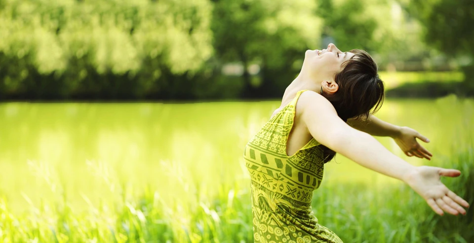 Woman stretching her arms wide in a sunlit green park