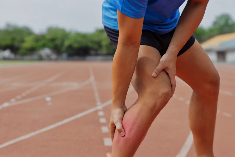 Runner clutching a strained calf muscle on an athletics track