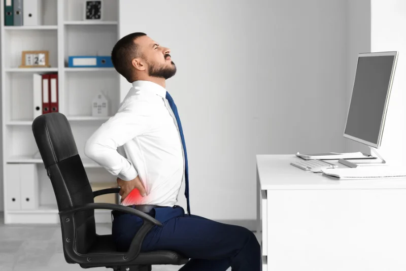 Office worker holding his lower back in pain at his desk